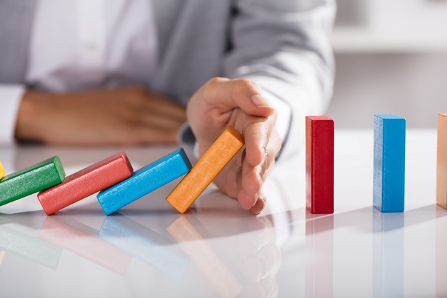 Close-up Of Businessperson Hand Stopping Colorful Blocks From Falling On Table In Office